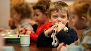 Kleuter zit huilend met knuffel in de hand aan de eettafel