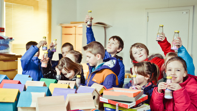 kinderen vullen flesjes met gekleurd zand