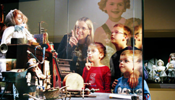 Mama met kinderen kijken naar vitrine met oude poppen en speelgoed