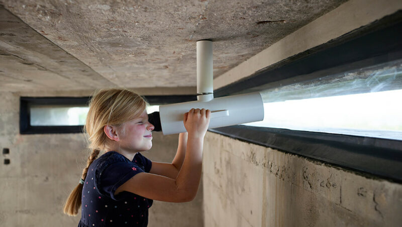 Meisje kijkt door verrekijker in bunker
