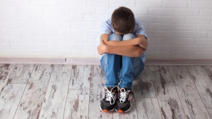 jongen zit in elkaar gedoken tegen een muur