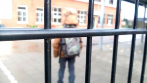kind op speelplaats, gezien door de schoolpoort