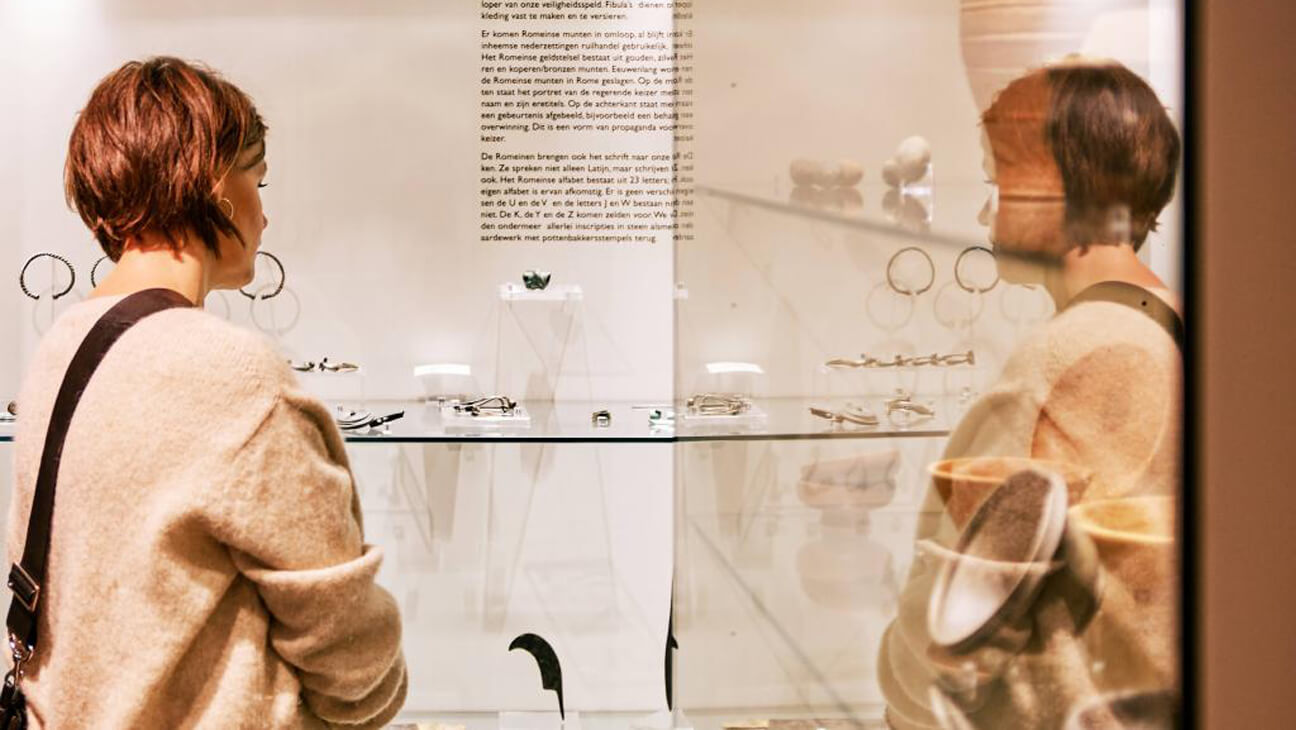 Vrouw kijkt naar vitrine in museum in Regionaal Archeologisch Museum Maaseik
