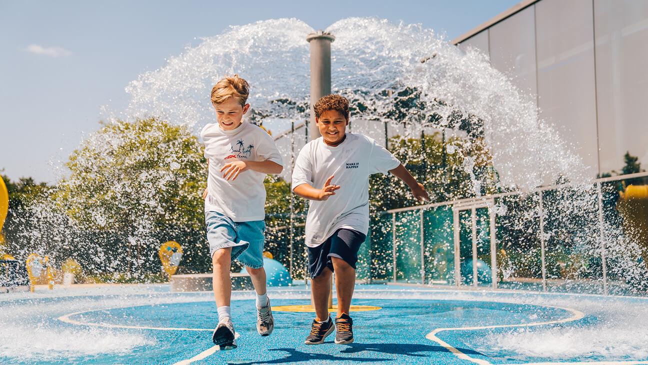 2 jongens lopen door een fontein in Hidrodoe, interactief waterdoecentrum