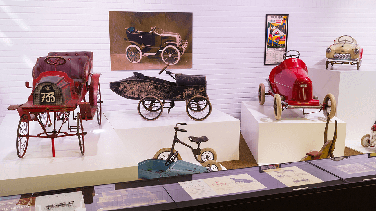 Oud speelgoed in een zaal van zicht op de gevel van Mudel, Museum van Deinze en de Leiestreek
