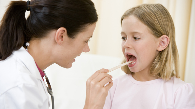 Dokter controleert jong meisje met tongspatel in onderzoeksruimte