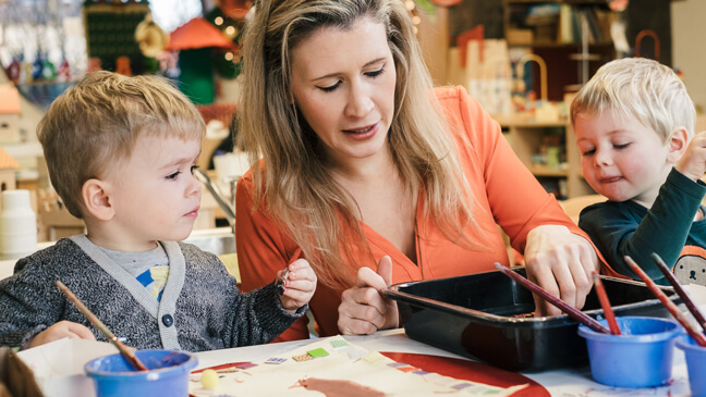 Juf Ellen werkt samen met 2 kleuters aan een knutselopdracht