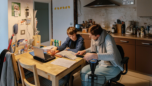 meisje aan tafel met mama in rolstoel