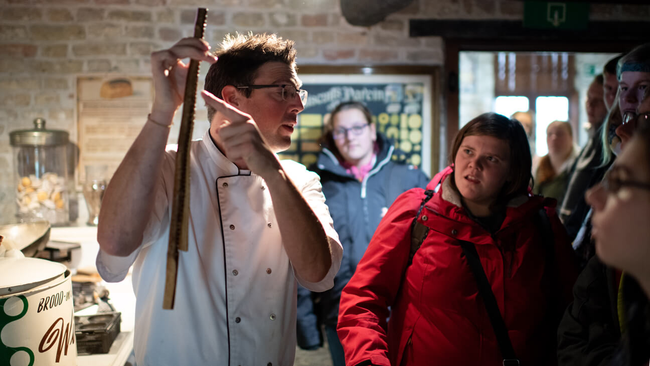 Bakker toont mal voor speculaas tijdens klasbezoek aan Bakkerijmuseum in Veurne