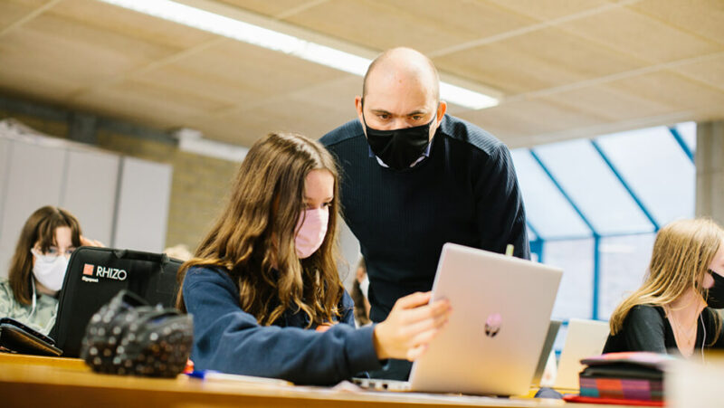 leraar Maarten De Vos in de klas met een leerling op haar laptop