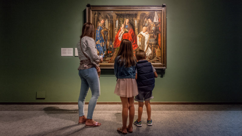Gezin kijkt naar een schilderij van Jan van Eyck in het Groeningemuseum
