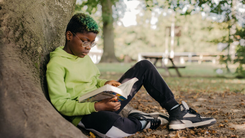 Jongen is boek aan het lezen onder boom op speelplaats