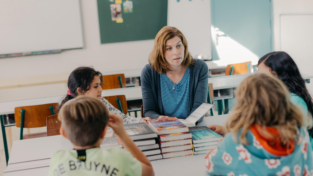 Leraar Jill met enkele leerlingen rond stapels boeken ivm begrijpend lezen op basisschool
