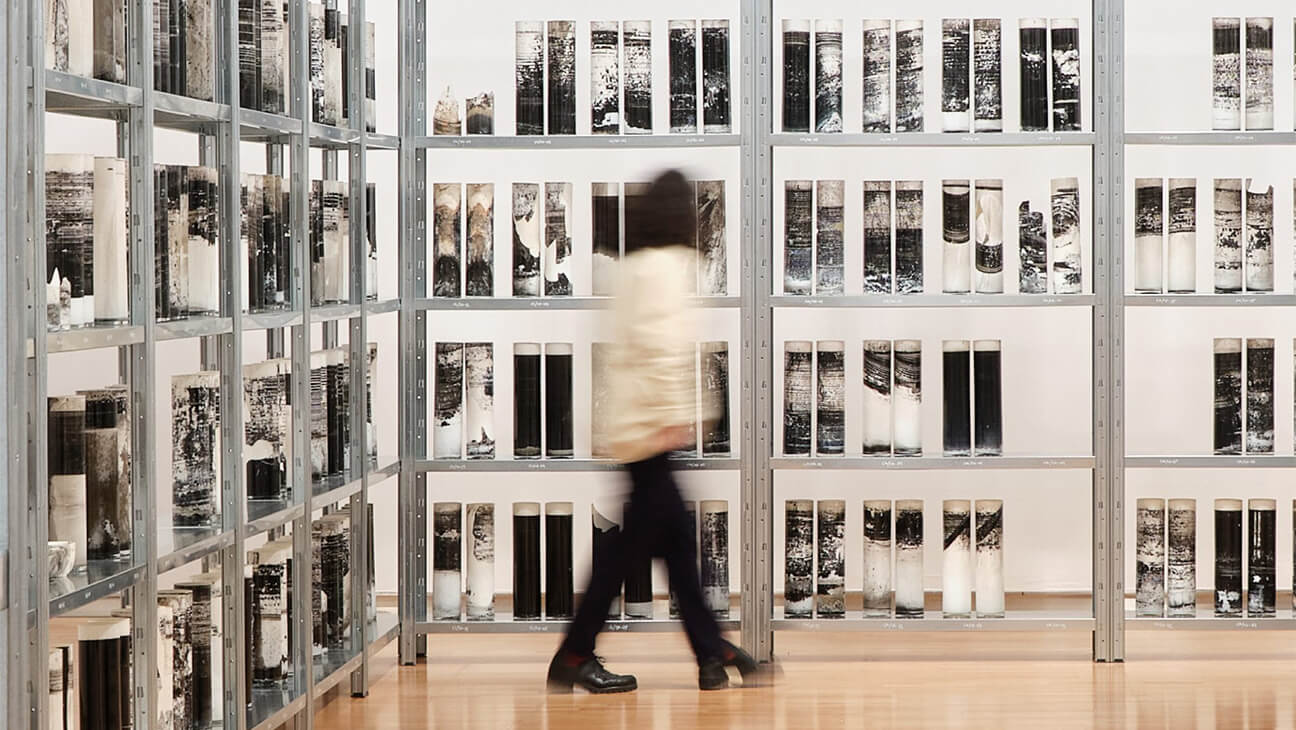 Bezoeker in een zaal met verweerde glazen cilinders  op de expo 'Biblioteca Nacional'
