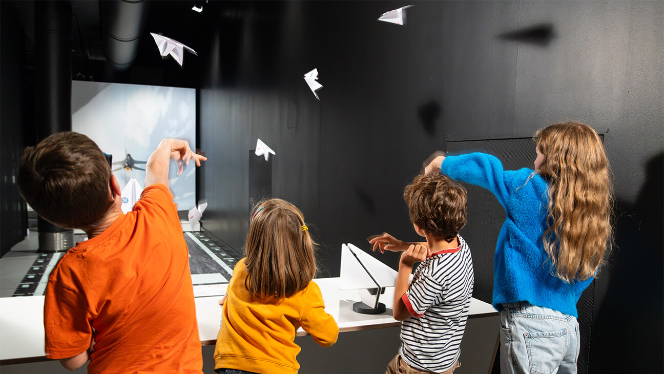 Kinderen gooien met een papieren vliegtuigje tijdens de expo 'Flight'