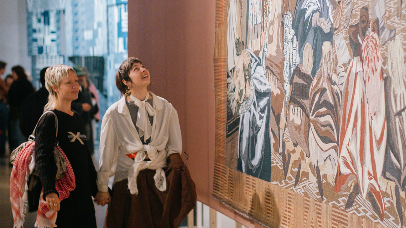 Bezoekers kijken naar een wandtapijt van Kunstenaar Sammy Baloji