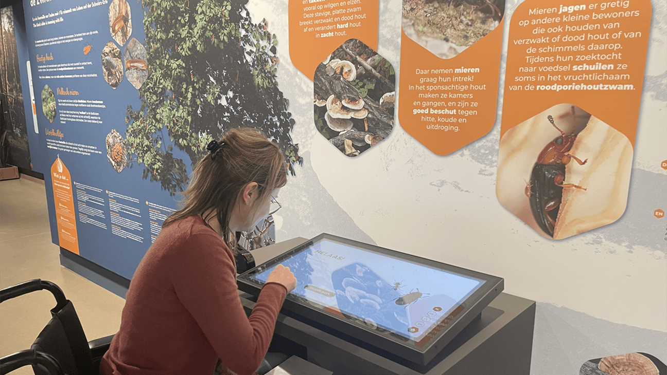 Meisje in rolstoel scrolt op groot scherm in insectenmuseum