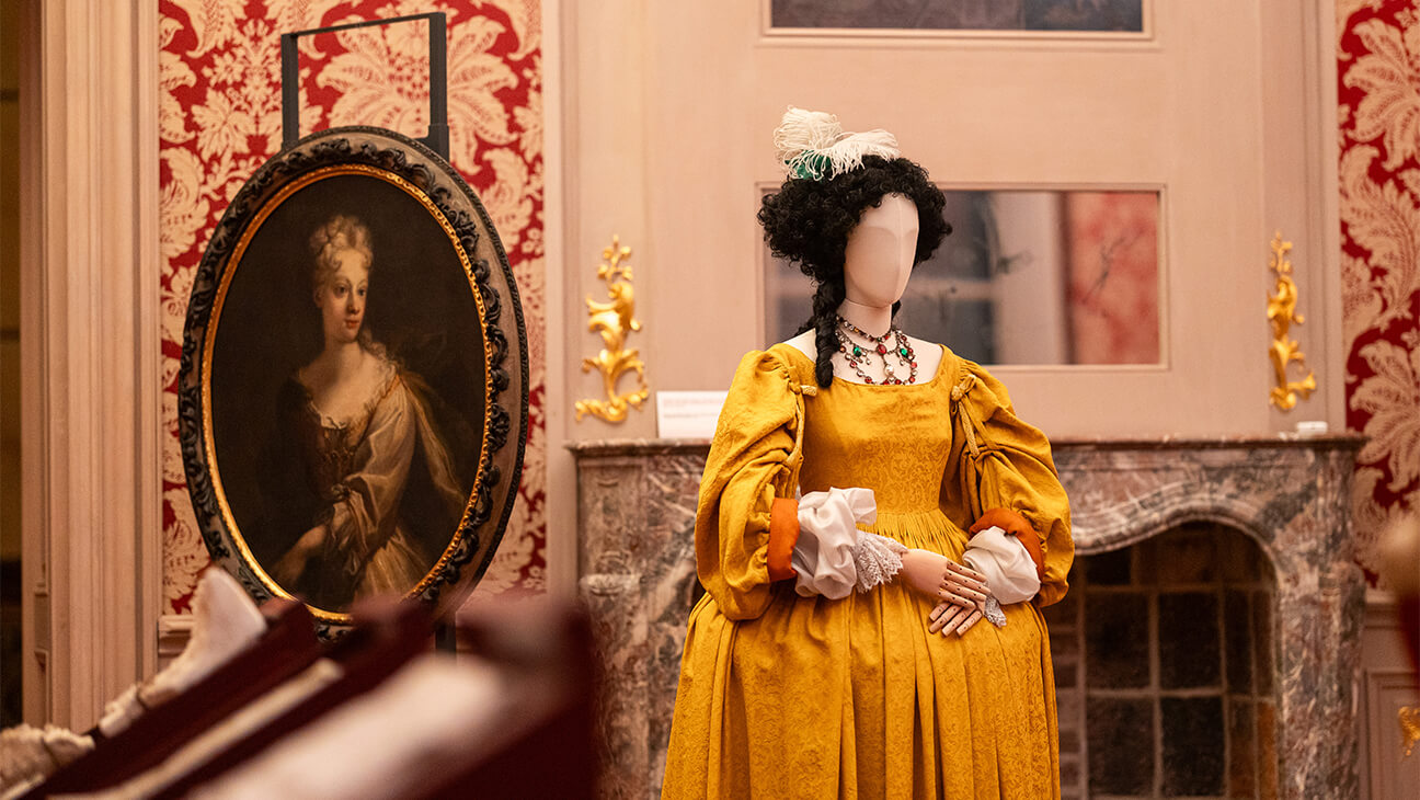 Oud schilderij van een vrouw naast een mannequin met een geel kleed