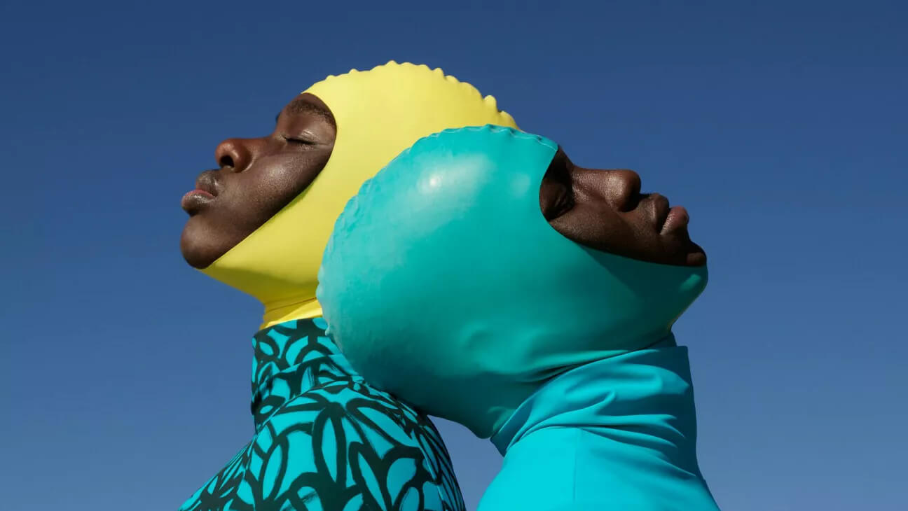 2 mensen met gele en groene badmuts met hun hoofd tegen elkaar